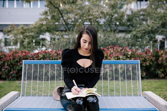Стильна жінка-підприємець сидить на лавці і робить нотатки в організаторі під час роботи в міському парку — стокове фото