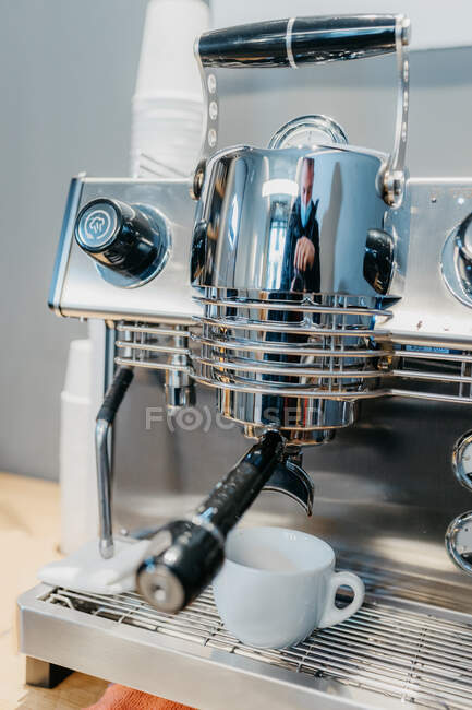 Современный профессиональный кофеварка наливая свежий горячий кофе в белый стакан в кафе в дневное время — стоковое фото