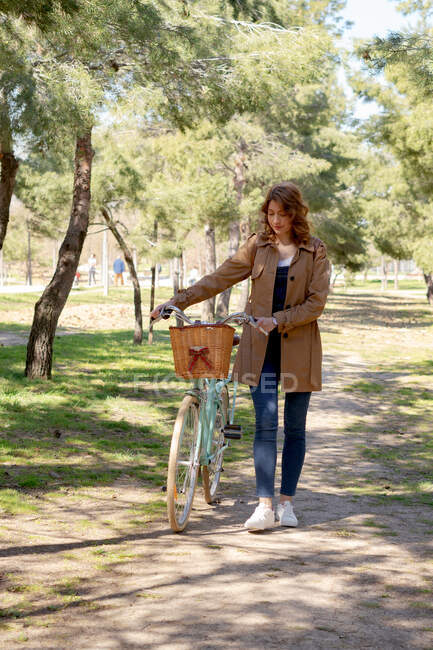 Corps complet de jeunes femmes marchant et concentrées près de vieux vélos avec panier en osier dans le parc — Photo de stock