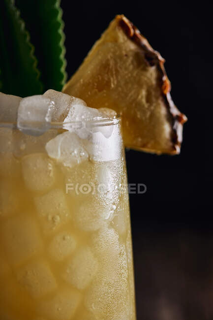 Дерев'яний стіл зі склянкою жовтого коктейлю з кубиками льоду та освіжаючим коктейлем, прикрашеним пряним листям та смугастою соломою — стокове фото