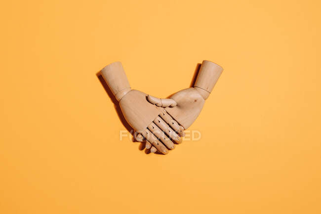 Верхний вид деревянных рук с рукопожатием в знак соглашения помещен на желтый фон — стоковое фото