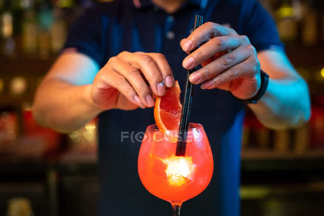 Imagen de las manos del joven camarero decorando un cóctel con cuña de pomelo y pajitas en el bar - foto de stock