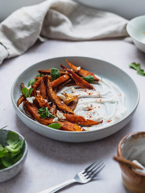 High angle of delicious sweet potato fries with sour cream and herbs served on table — Stock Photo