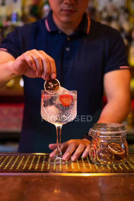 Unrecognizable bartender decorating a gin tonic cocktail with a slide of dry lemon in the bar — Stock Photo