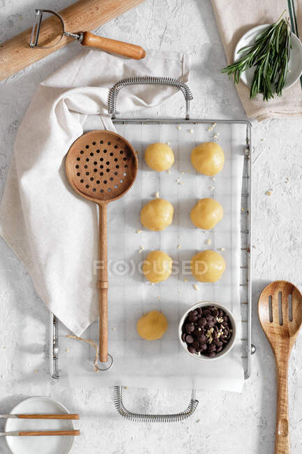 Top view of sweet cookie dough in shape of balls placed on baking paper on table with chocolate chips and rosemary branches before baking — Stock Photo