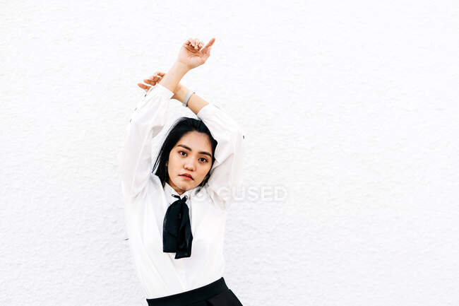 Serious ethnic female in uniform keeping hands crossed over head standing against white background and looking at camera — Stock Photo