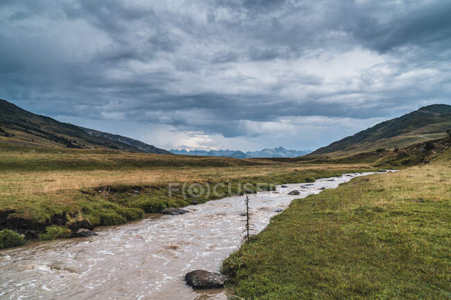 Ruisseau au milieu d'une prairie sans fin avec de l'herbe verte fraîche sous le ciel avec des cumulus — Photo de stock