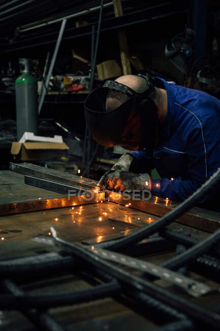 Обрізання безликого робітника в рукавичках і рівномірні деталі зварювального металу на столі поблизу будівель на заводі — стокове фото