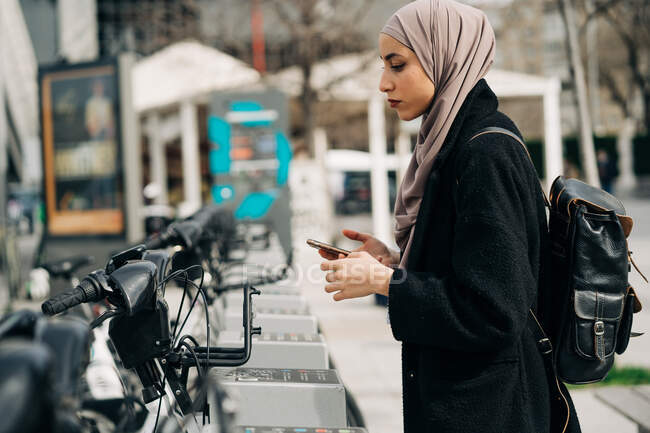 Seitenansicht einer Muslimin mit Kopftuch beim Fahrradverleih in der Stadt — Stockfoto