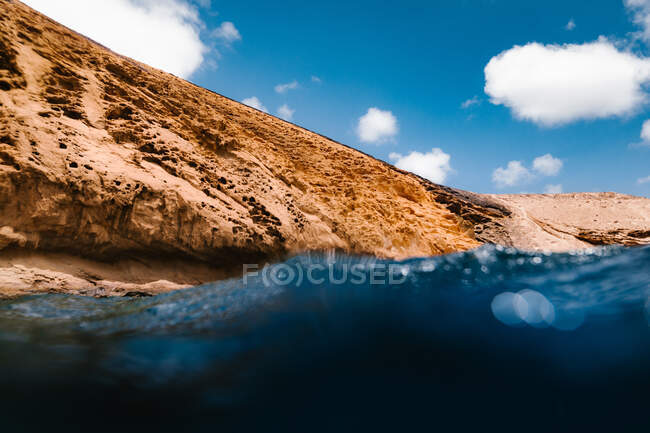 Низький кут чистої морської води, що миє скелясту скелю на узбережжі під блакитним небом з хмарами — стокове фото