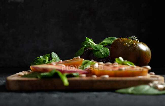 Fresh ripe sliced black tomatoes and green mint stems on wooden cutting board on black background — Stock Photo