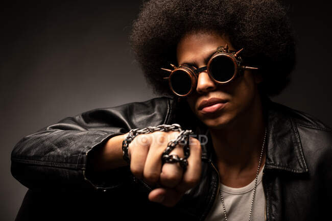 Trendy African American male in leather jacket and contemporary sunglasses with Afro hairstyle on gray background — Stock Photo