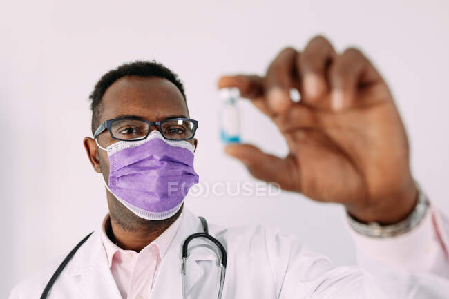 Uomo afroamericano in uniforme con stetoscopio che mostra vaccino sfocato in mano in ospedale — Foto stock