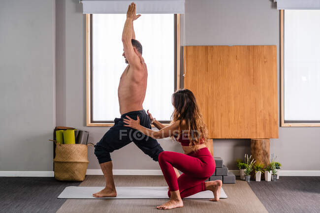 Vista laterale del trainer femminile concentrato in abbigliamento sportivo che insegna all'uomo a eseguire una posa ad alto affondo durante la sessione di yoga in studio — Foto stock
