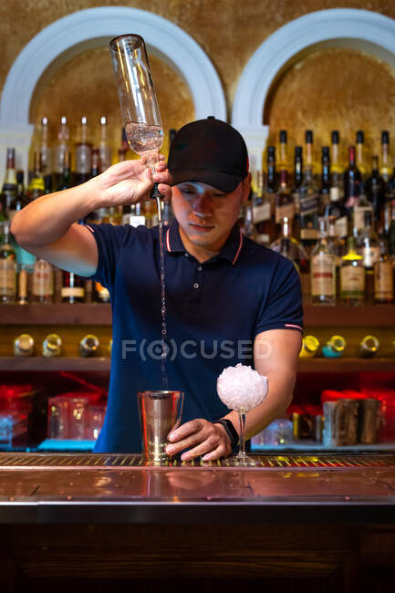 Joven camarero asiático vertiendo vodka en la coctelera mientras prepara un cóctel en el bar - foto de stock