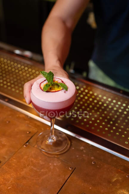 Mains de barman méconnaissable servant un cocktail avec des feuilles de menthe et des fruits de la passion dans le bar — Photo de stock