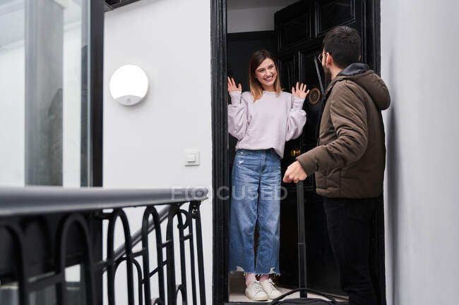 Cheerful young lady meeting anonymous boyfriend with luggage returned from business trip on doorstep of house — Stock Photo