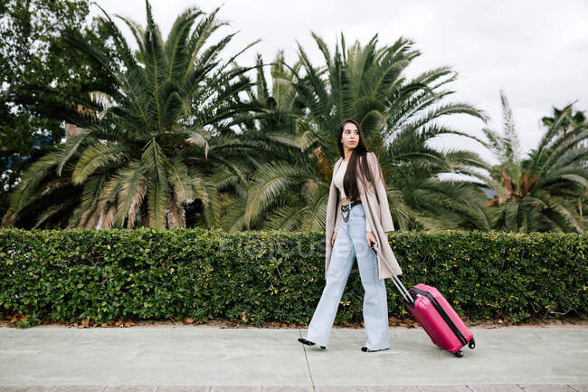 Selbstbewusste Unternehmerin in stylischer Kleidung läuft mit Koffer die Stadtstraße entlang und schaut weg — Stockfoto