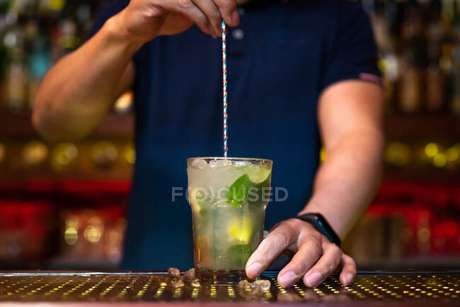 Camarero irreconocible sosteniendo el vaso y revolviendo cóctel mojito en el bar - foto de stock