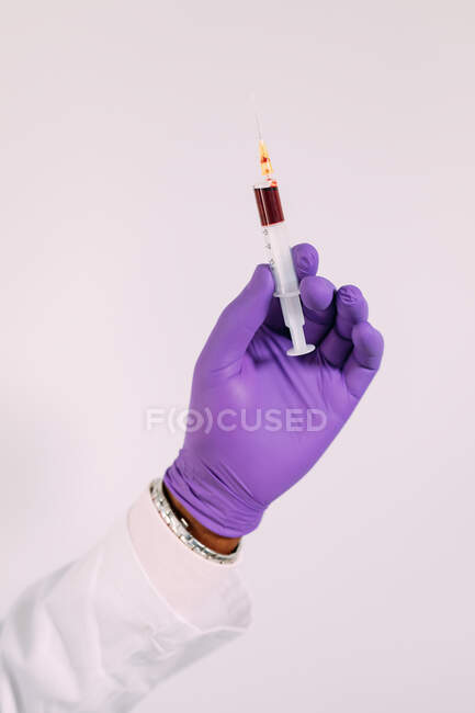 Cultiver médecin anonyme dans un gant médical démontrant seringue avec du sang sur fond blanc — Photo de stock