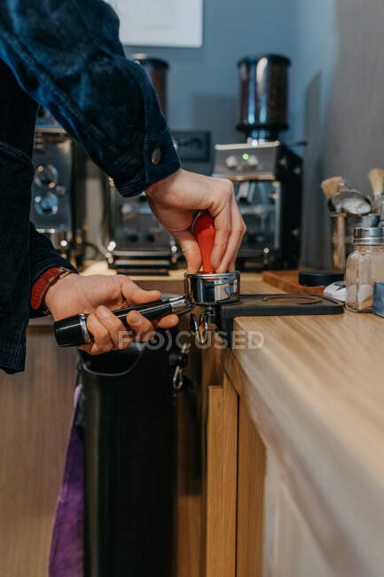 Обрежьте безликого бариста, стоящего за столом и готовящего свежий ароматический кофе, работая днем в кафетерии — стоковое фото