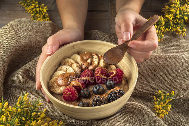 Анонимный повар урожая показывает миску с банановыми ломтиками и разнообразные свежие ягоды с карамельным соусом на завтрак — стоковое фото
