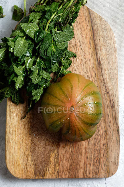 Зверху свіжого смугастого зеленого і червоного помідорів кладуть на дерев'яну обробну дошку з купою м'ятних стебел — стокове фото