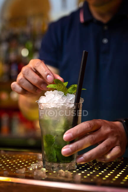 Руки невпізнаваного бармена, що прикрашає мохіто коктейль з листя м'яти в барі — стокове фото