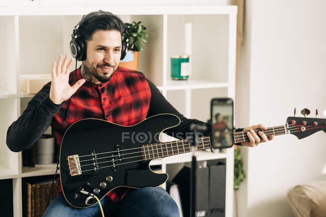 Stativ mit Handy-Bildschirm, der die Fotografie eines männlichen Musikers im Headset darstellt, der im Haus Bassgitarre spielt — Stockfoto