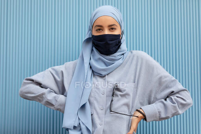 Jeune musulmane auto-assurée en tissu masque facial avec les mains sur la taille en regardant la caméra en plein jour — Photo de stock