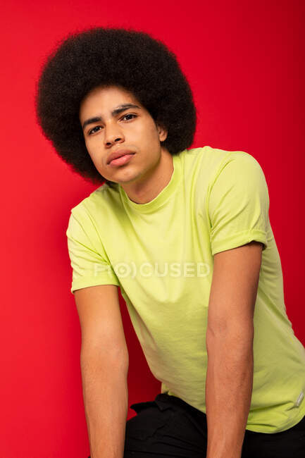 Junger selbstbewusster Afroamerikaner in lässigem T-Shirt blickt in die Kamera auf rotem Hintergrund — Stockfoto
