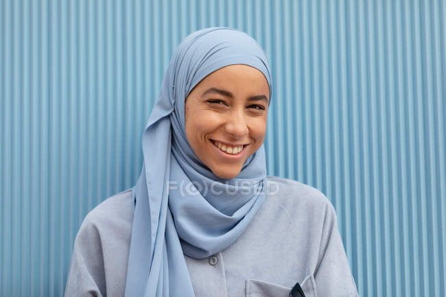 Jovem muçulmana solitária com olhar melancólico olhando para a câmera contra a parede nervurada durante o dia — Fotografia de Stock
