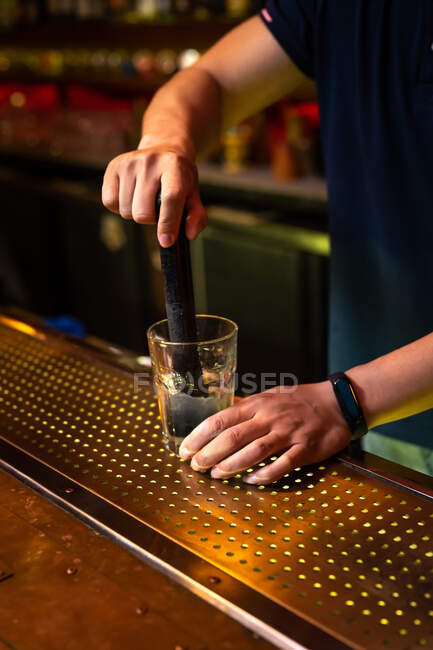Unrecognizable bartender crushing lemon wedges in the glass while preparing mojito cocktail in the bar — Stock Photo