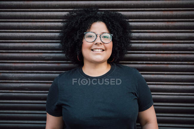 Content adult overweight female in eyewear curly hair against ribbed wall in daytime — Stock Photo
