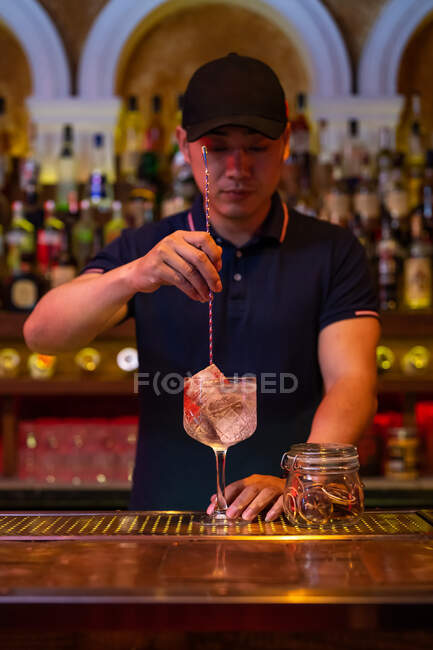 Junger asiatischer Barkeeper rührt einen Gin Tonic Cocktail mit einem Löffel in der Bar — Stockfoto