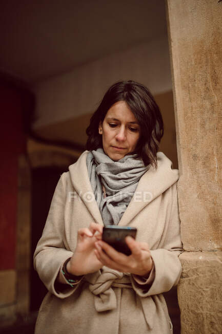 Vista frontal da fêmea em pé em mensagens de texto outerwear no celular — Fotografia de Stock