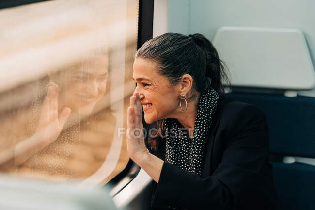 Side view of positive female waving hand and looking out window while sitting on passenger seat in wagon during ride — Stock Photo
