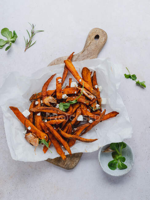 Top view of tasty sweet potato fries with green corn salad and rosemary served on wooden chopping board on table — Stock Photo