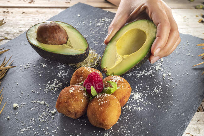 From above of crop anonymous cook with ripe avocado halves near appetizing deep fried croquettes with raspberry on top — Stock Photo