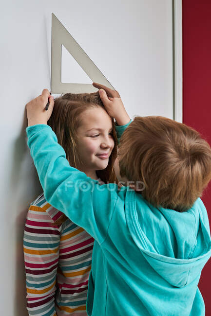Fratello aiutare sorella con la misurazione della sua altezza con righello e matita vicino al muro — Foto stock
