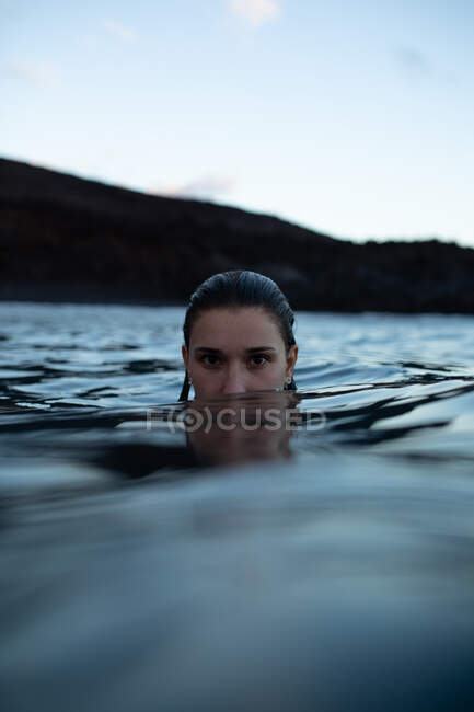 Viaggiatore femminile nuotare in acqua pulita blu contro scogliera rocciosa durante il viaggio guardando la fotocamera — Foto stock