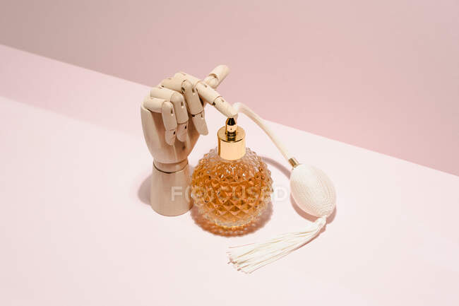 Стильна прозора пляшка парфумів, розміщена між дерев'яною рукою, розміщена на рожевому фоні в світлій студії — стокове фото
