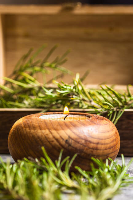 Bougie aromatique brûlante dans un chandelier près d'une petite poitrine en bois remplie de branches de romarin avec des feuilles vertes sur la table — Photo de stock