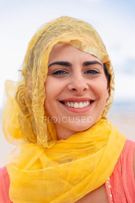 Joven mujer alegre con sonrisa dentada mirando a la cámara sobre un fondo borroso de cielo nublado - foto de stock