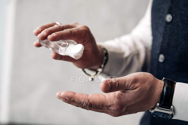 Crop empresario masculino anónimo en desgaste formal y reloj de pulsera con gel desinfectante de botella durante el período coronavirus - foto de stock