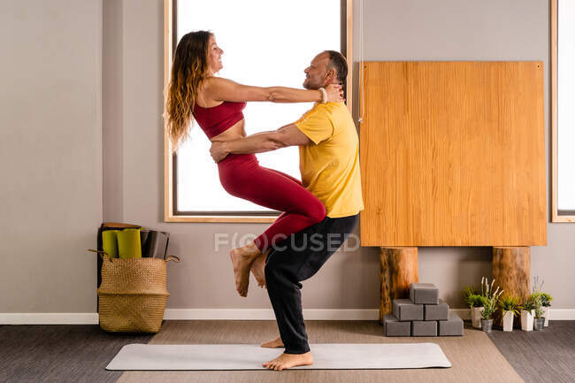 Vista lateral de pareja positiva en ropa deportiva realizando yoga asana juntos mientras practican yoga en casa a la luz del día - foto de stock