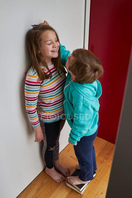 De arriba del hermano que mide la altura del contenido la hermana que está parada cerca de la pared en la habitación - foto de stock