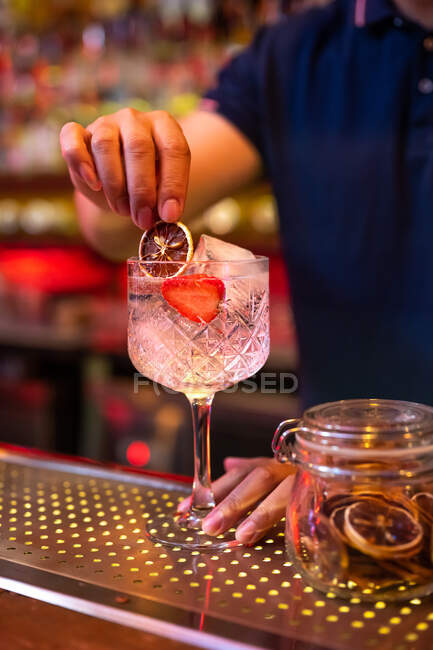 Unrecognizable bartender decorating a gin tonic cocktail with a slide of dry lemon in the bar — Stock Photo