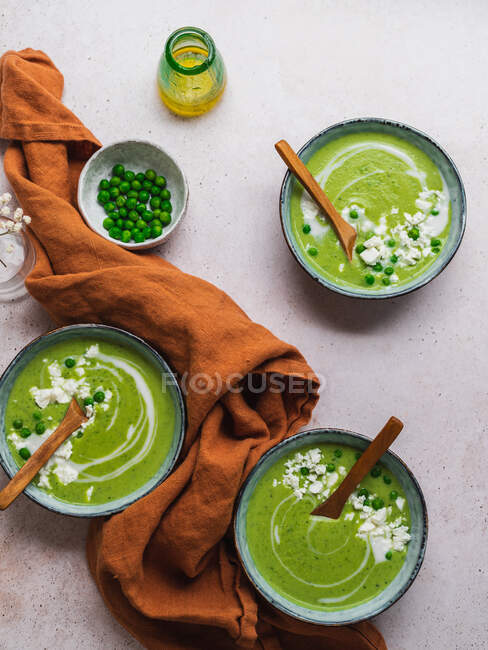 Top view of delicious pea cream soup in bowls served on table with napkin and vase with flowers — Stock Photo
