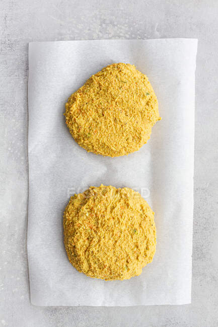 Top view of raw homemade veggie chickpea and curry cutlets in bread crumbs for burger on parchment sheet on gray background — Stock Photo